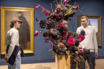 Wilhelm Schmurr: Bildnis Werner Heuser, 1902, floral interpretiert von Christina Janet Schacke, 
Blumenhaus am Hofgarten
: Gegen den Strom mit 
<i>Vanda</i>
, 
<i>Calla</i>
, 
<i>Scabiosa </i>
und Aubergine