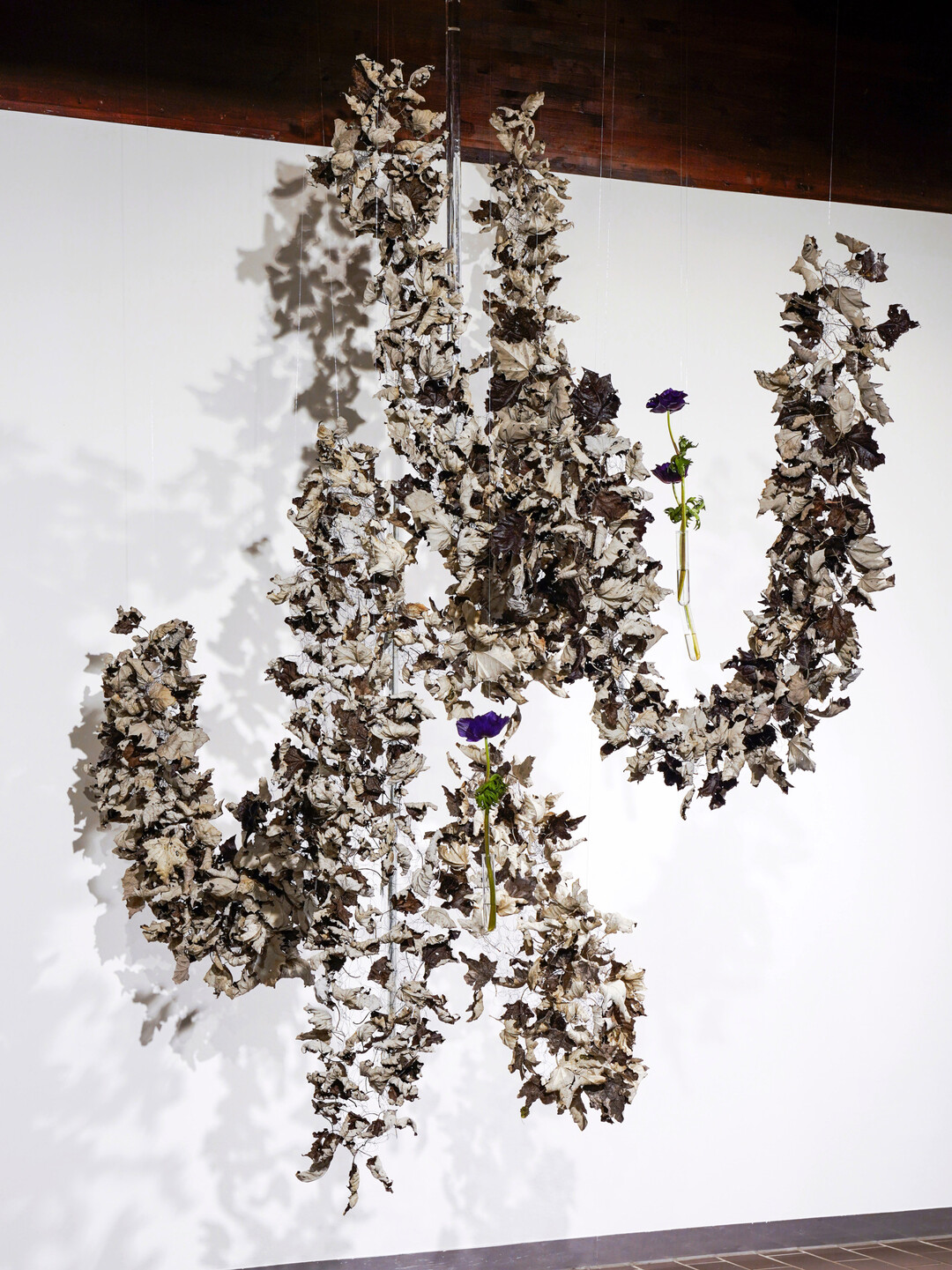 Ein Spiel mit Licht und Schatten zeigt das Werkstck von 
<b>Neele Malaa.</b>
 Die Oberseite der Silberpappelbltter ist graubraun, dunkel, doch die Unterseite in weichem Silbergrau wlbt sich im Trocknungsprozess nach oben und tritt in den Vordergrund. Die Metallstange ersetzt Neele durch zwei Glasstangen, die wie schmelzende Eiszapfen zwischen den Blttern hngen. Samtige Anemonen in dunklem Violett runden die Gestaltung ab. 