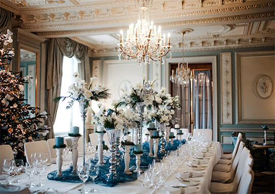 Der Salon Bleu ist einer der beliebtesten Rume des Grand Hotels. Beim Lichteinfall strahlen die vielen Ornamente und Details in besonderem Glanz. Er eignet sich fr die Weihnachtsfeier einer hochrangigen Schweizer Familie. Der 3,5 m hohe Baum wurde noch speziell fr diesen Abend aufgebaut. Die Tafel war das Highlight des Abends. Neben den Blumen, die die Farben des Raums widerspiegeln, spielt Licht eine groe Rolle. Kerzen sind ein wichtiges Gestaltungselement und Lichterketten unter dem Stoff bringen auch abends den Glanz des Raums und die Feinheiten der Deckenarbeiten zur Geltung.