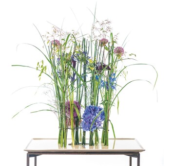 Diese Arbeit ist eine Sammlung von Bndeln aus Grsern und Blten mit beinbewussten Stielen wie Allium, Agapanthus und Zantedeschia. Auch die Schachtelhalme steuern Bndelmasse bei. Dass Blaues weitgehend unter sich bleibt, ist so eigentlich nur im Sommer machbar. Gehalten wird das Ganze durch eine Konstruktion aus Draht, die eher tektonisch symmetrisch aufgebaut ist  sehr stabil und mit