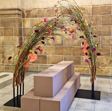 Die gebogene Anordnung, die den Sarg umgibt, stellt Bewegung und Freiheit dar � wie es auch bei einer T�nzerin auf der B�hne der Fall w�re. Zwei Metallplatten und darauf geschwei�te Rohre dienen als technische Basis. Die Weide dient sowohl als geschwungenes Gestaltungselement als auch als technische Basis f�r die Blumen. Eine freie Anordnung der passend ausgesuchten Bl�ten verst�rkt die Aussage des Sargschmucks.