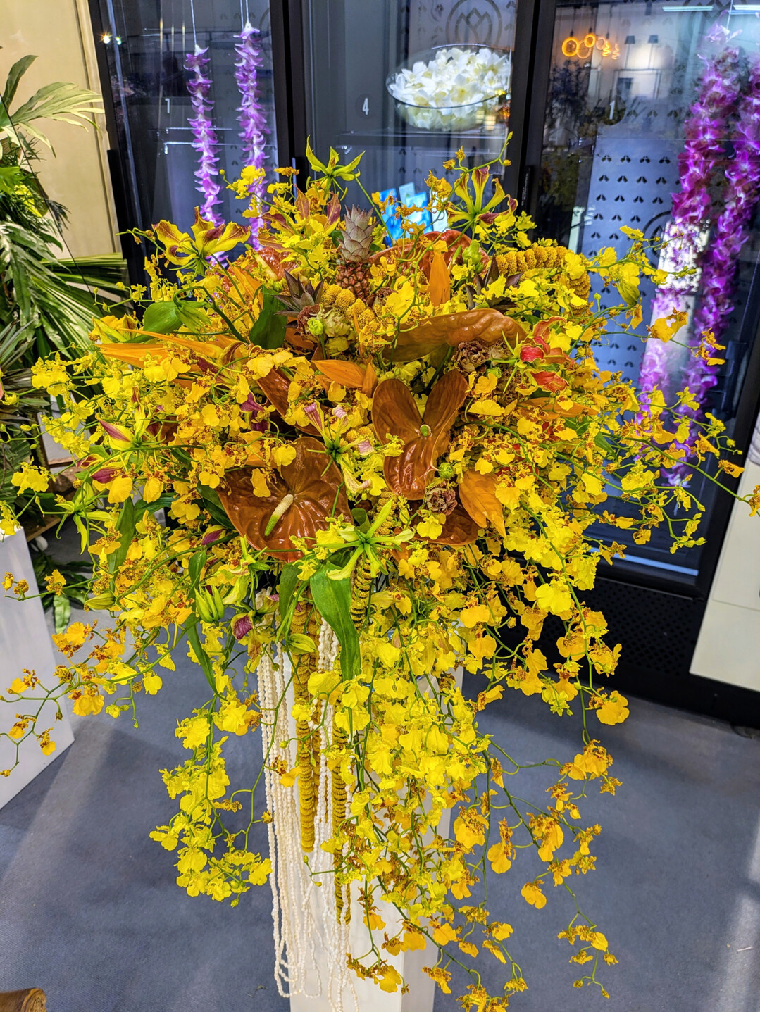 Ein Strau�, der mit der Sonne um die Wette leuchtet. Ketten aus aufgef�delten Chrysanthemen und Muscheln kommen auch hier zum Einsatz und verst�rken den abflie�enden Charakter der 
<i>Oncidium</i>
-Rispen.  