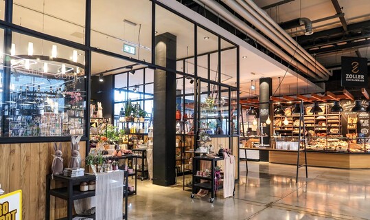 1) Nach der Schlieung eines Restaurants vergrerte sich der Bcker etwas und es wurde ein Nachfolger fr die leerstehende Flche gesucht. Durch verglaste Wnde getrennt, schliet der Cafbereich nun an die Stilfabrik an. Das Blumengeschft lsst sich durch v erschliebare Tren vom brigen Areal abtrennen. Das ermglicht abweichende ffnungszeiten, das Arbeiten an Sonntagen und Betriebsurlaube.
