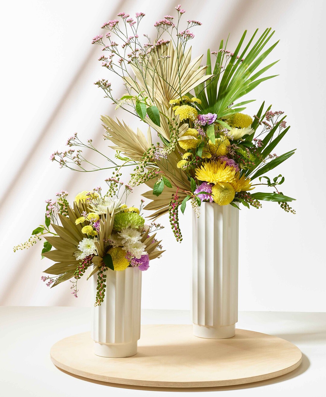 Riviera Roadtrip: Das Duo mit aufstrebenden Palmenblttern und auffllig-gestaffeltem Aufbau ist ein trendiger Eyecatcer. Chrysanthemen fgen sich eher gefllig ein und runden die floralen Skulpturen ab.