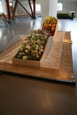 Die Interpretation des Zitats von Erich Maria Remarque: "Das Wunder, wenn man es erlebt, ist nie vollkommen. Erst die Erinnerung macht es dazu." Ettle fertigte das wellenförmige Pflanzgefäß aus Holzplatten, die sie mit Kleister bestrich und mit Sand bestreute. Den Innenraum füllte sie mit Steckmasse. Zwischen die Wände gespannte Dyneema-Schnüre halfen beim Stecken des Wellenverlaufs. Unter die Schnüre verwebte Ettle rankende Pflanzen, wie Knöterich, Pfeifenwinde und Hopfen.