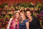 Sarah Wiener und Gesine Cukrowski posieren mit Diadem und Brosche vor der Blumenwand.